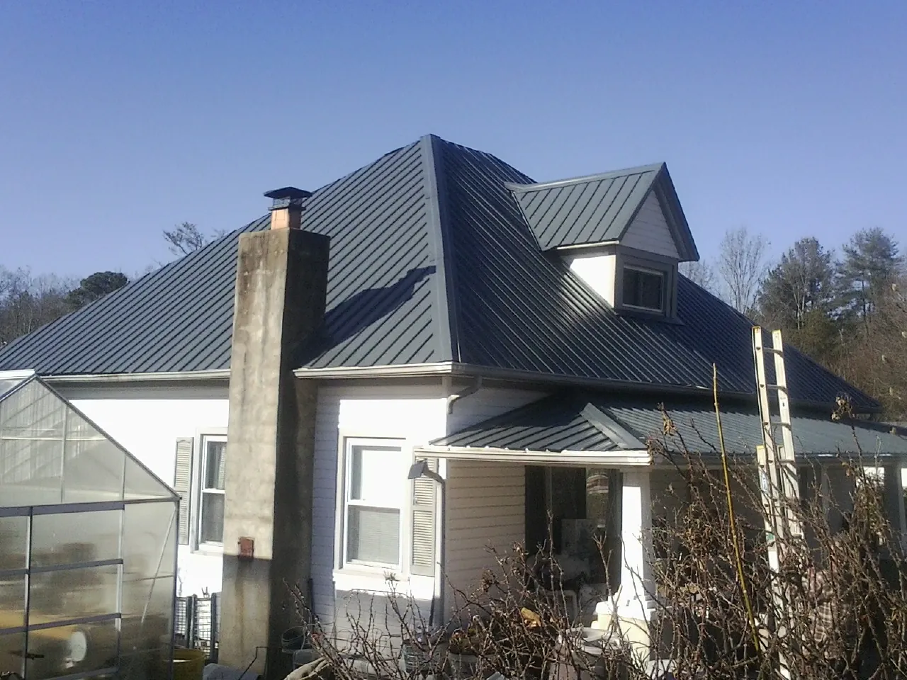 Dark blue standing seam metal roof on a white farmhouse with dormer — Slate & Tile Roof Repair by Roofing Brothers in Flournoy