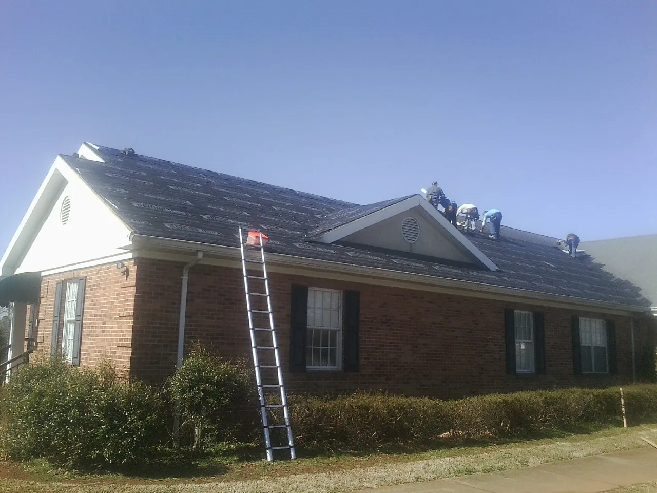 Crew tearing shingles off a brick ranch roof with a ladder set — Emergency Roof Repair work by our crew in Flournoy