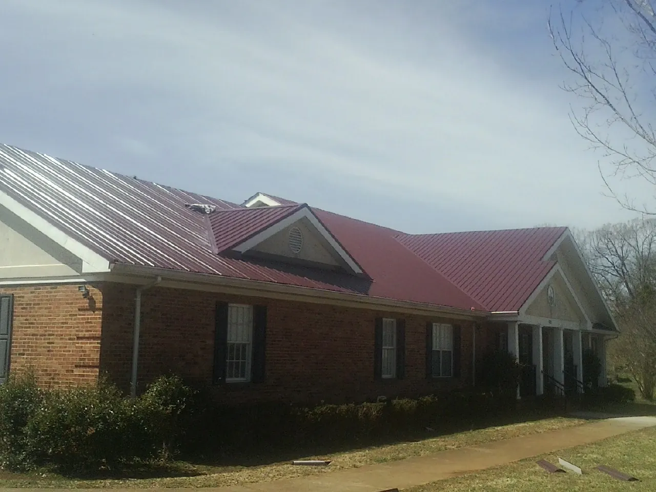 Red metal roof with gabled entries on a long brick building, from a Hail Damage Roof Repair job in Flournoy