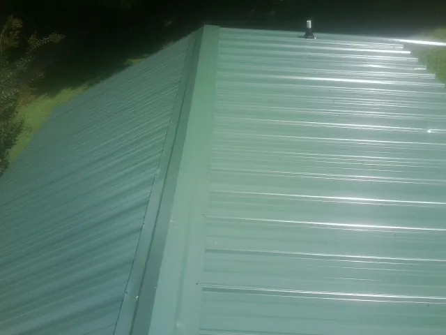 New green metal panels meeting at the ridge of a roof — Flat Roof Repair work by our crew in Flournoy