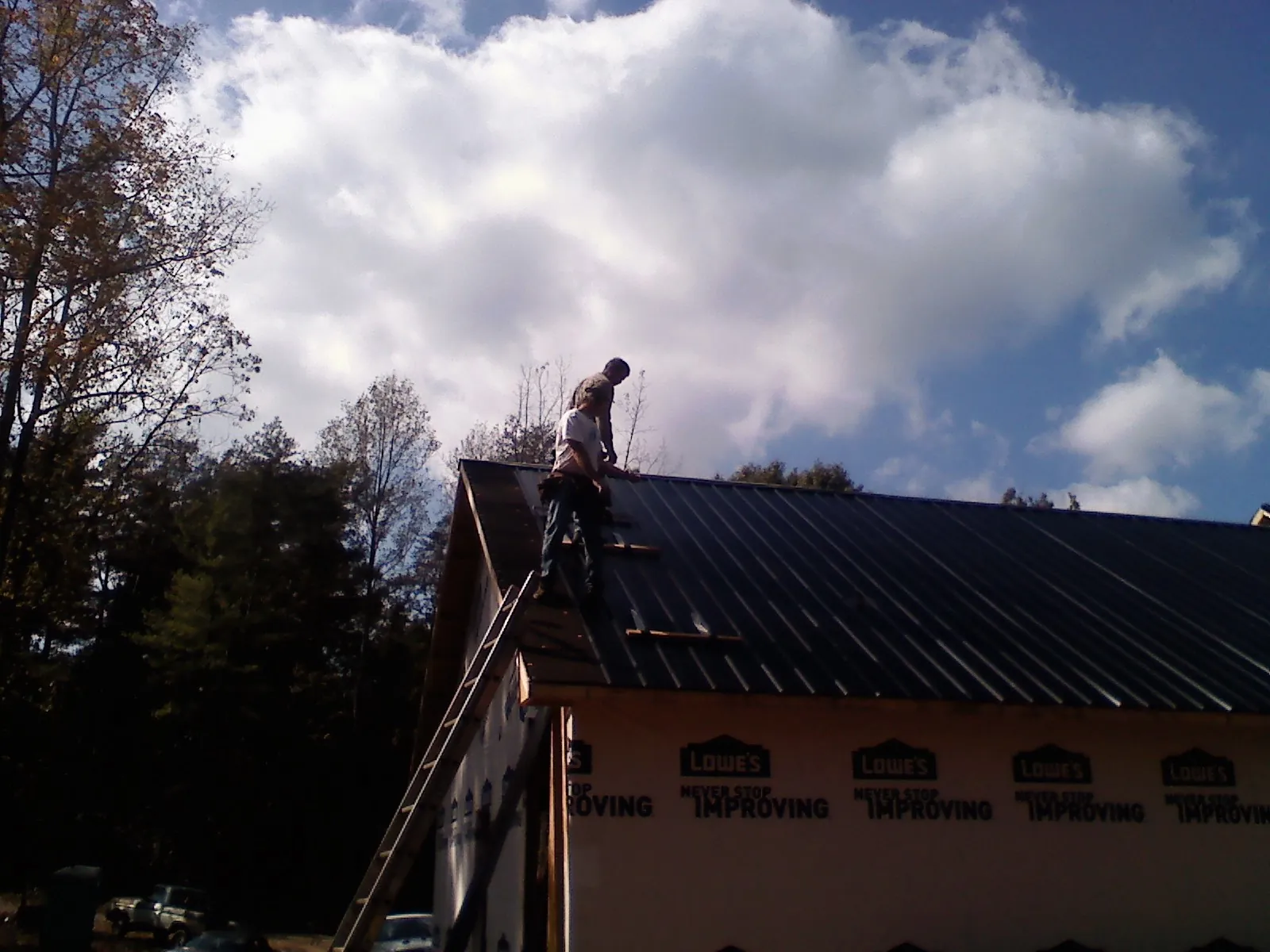 Roofer fastening dark metal panels high against a cloudy sky, from a Roof Inspection job in Flournoy