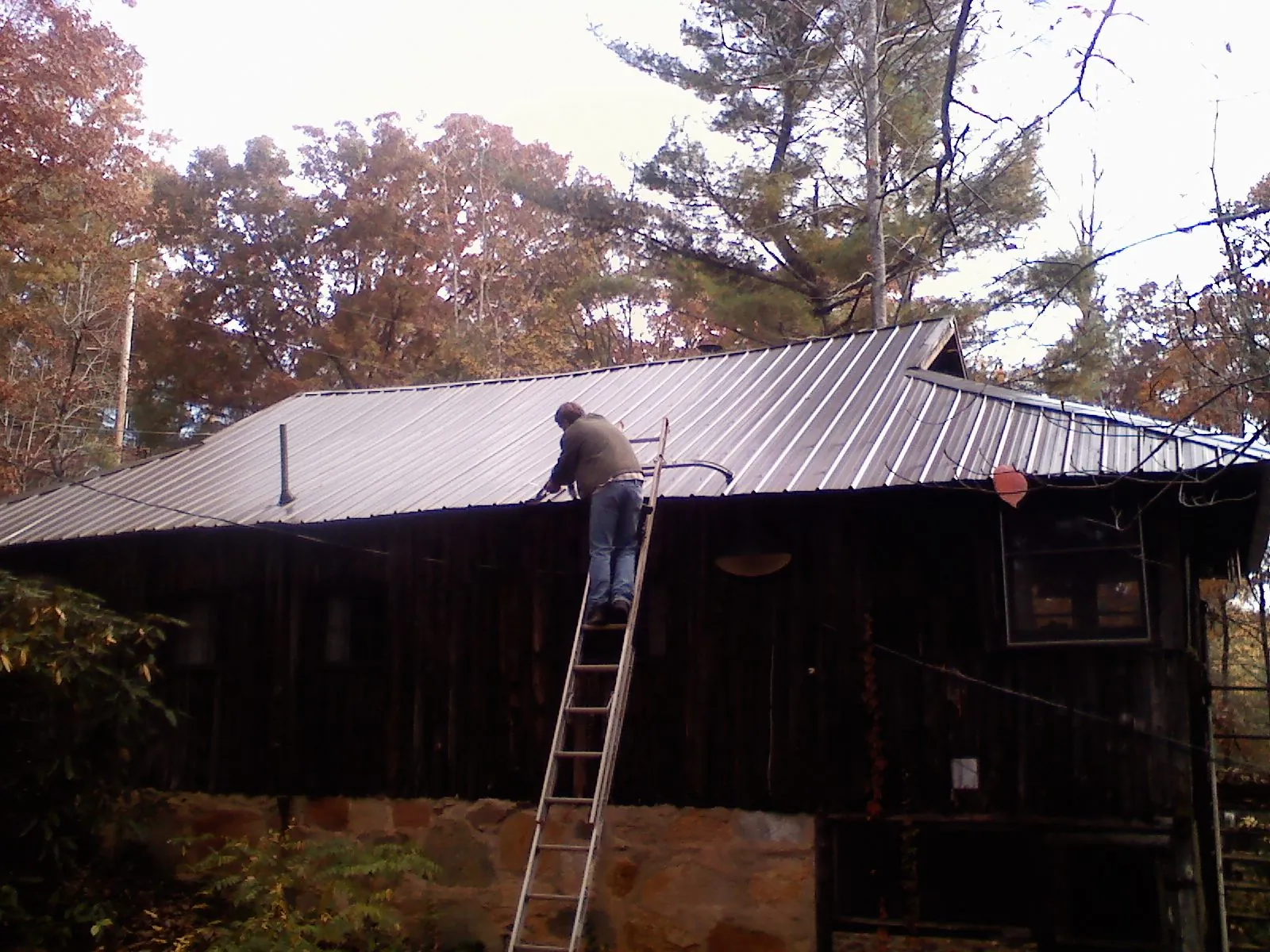 Roofer on a ladder working along the edge of a cabin metal roof in Flournoy
